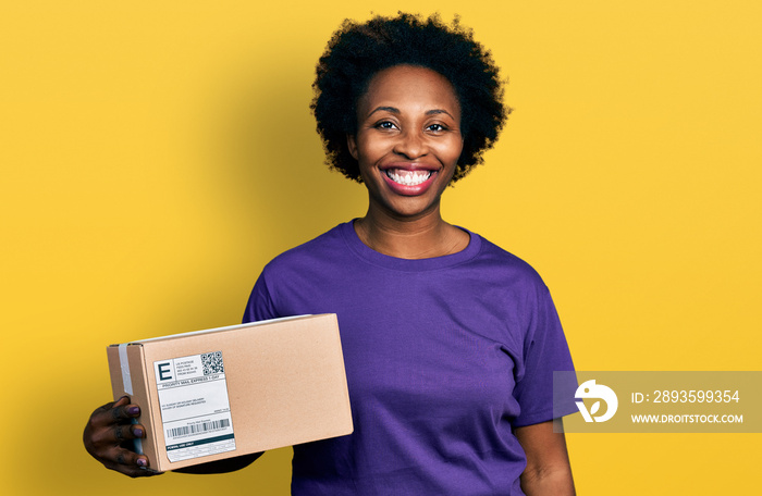 African american woman with afro hair holding delivery package looking positive and happy standing a