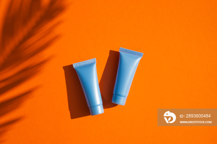 Two plastic blue bottles for cream or lotion with palm leaves shadow. Top view on orange background.