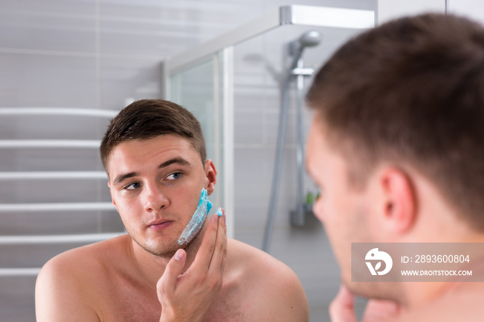 Handsome young man smearing shaving gel on his face