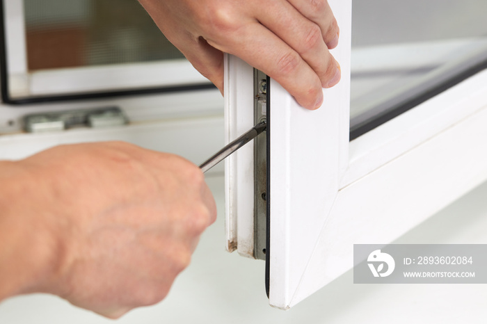 handyman adjusting white pvc plastic window indoors. worker using screwdriver to repair upvc window.