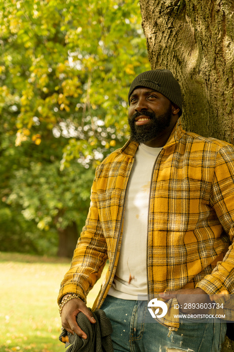 Smiling man leaning on tree trunk in park in autumn