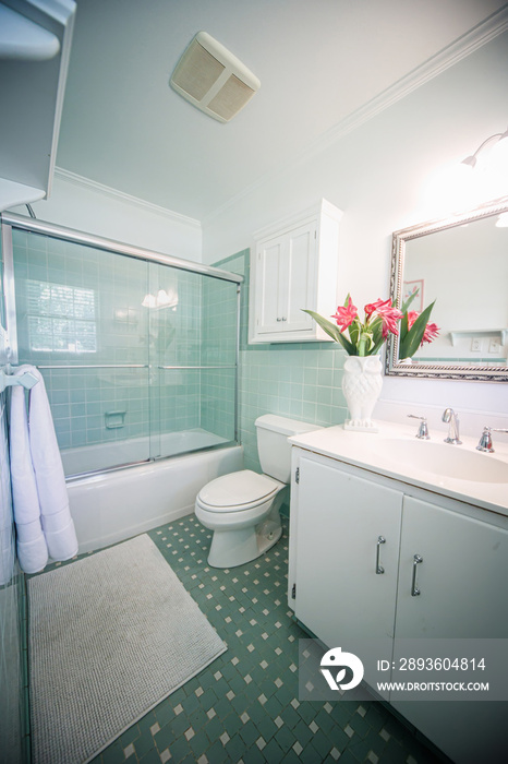 过时的瓷砖小浴室，配有透明玻璃门和白色橱柜水槽梳妆台和镜子