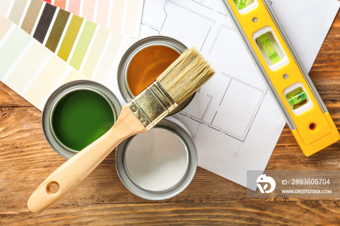 Cans of paint with supplies, palette samples and house plan on wooden table