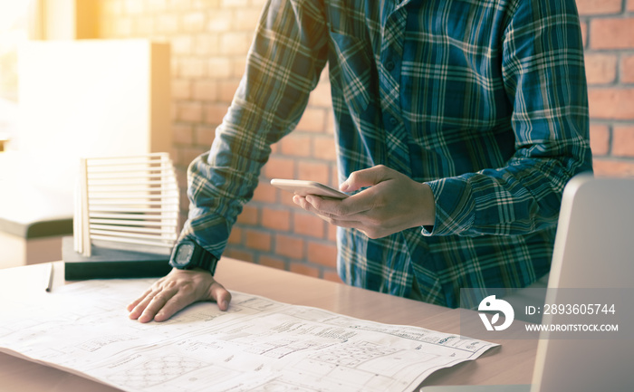 Architect standing typing on smartphone and working in modern office.