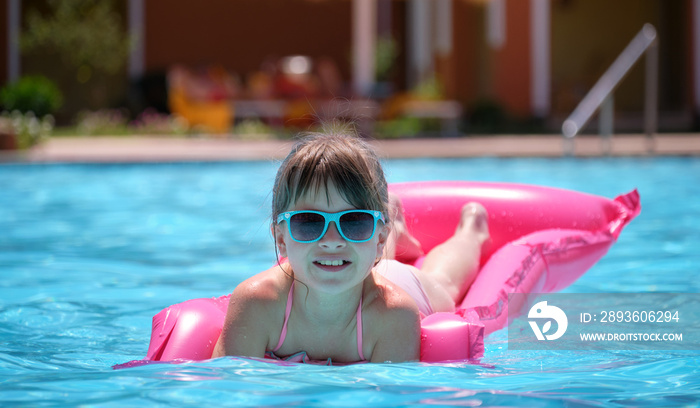 小女孩在夏日阳光下放松，在游泳池的充气气垫上游泳