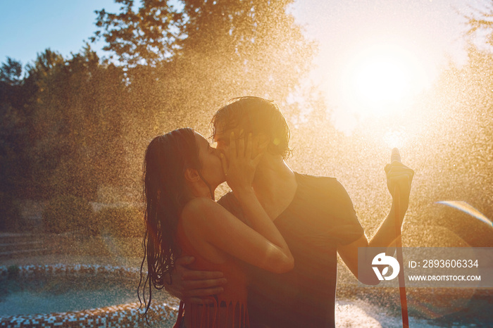 Couple having fun pour each other with garden hose