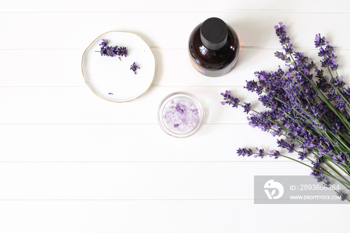 Styled summer beauty composition. Essential, massage oil, lavender flowers bouquet, bath salt on whi