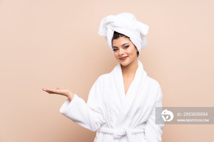 Teenager girl in a bathrobe over isolated background holding copyspace imaginary on the palm