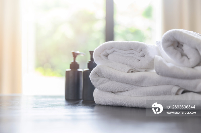 Roll up of white towels with shampoo bottles and liquid soap bottles on table with copy space on blu