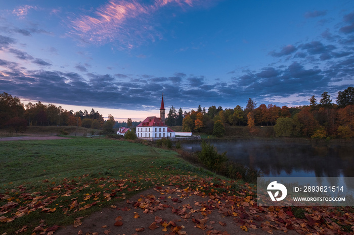 Prioratskiy Palace by the lake  in the city park of Gatchina, foggy morning during golden autumn.