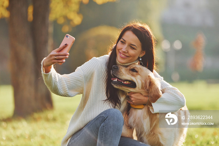 Making selfie. Young woman have a walk with Golden Retriever in the park