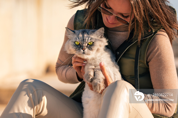 Stylish lady with her beautiful grey groomed persian chinchilla purebred cat sitting outside on the 