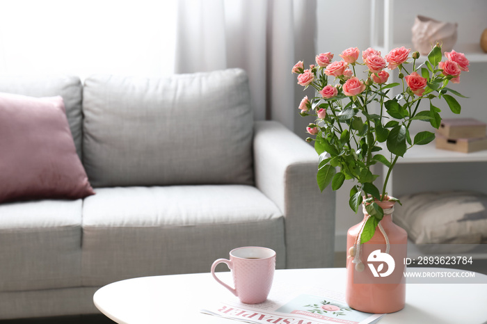 Vase with beautiful fresh roses and cup of coffee on table in room