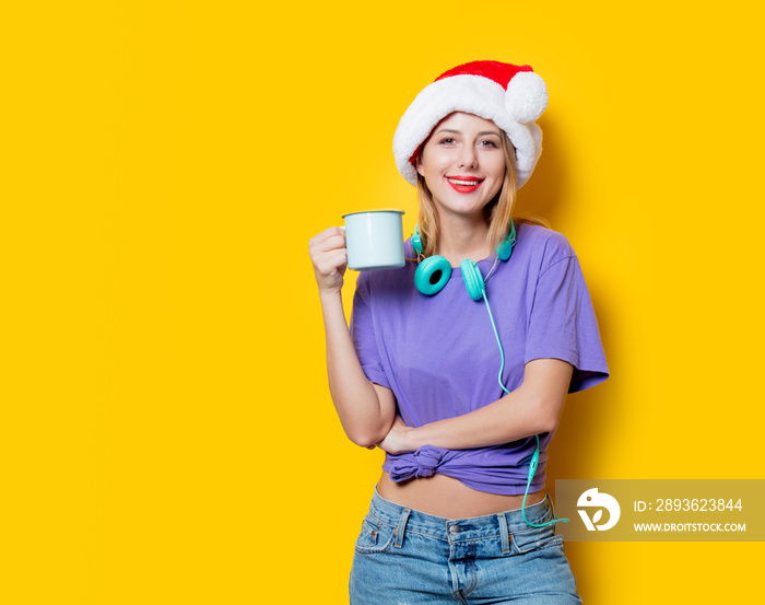 Young style girl in purple clothes and Christmas hat and cup on yellow background.  Clothes in 1980s