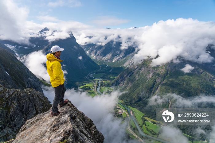 年轻的亚洲男子旅行者站在岩石上眺望群山，挪威罗姆斯代尔根徒步旅行道，