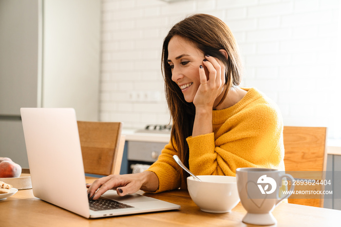 Beautiful woman using laptop computer while having breakfast at home