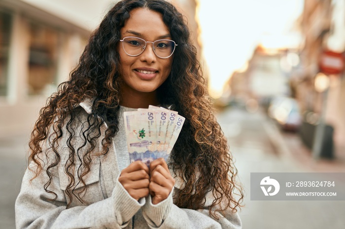 年轻的拉丁女人在城市里拿着哥伦比亚比索钞票，开心地微笑着。