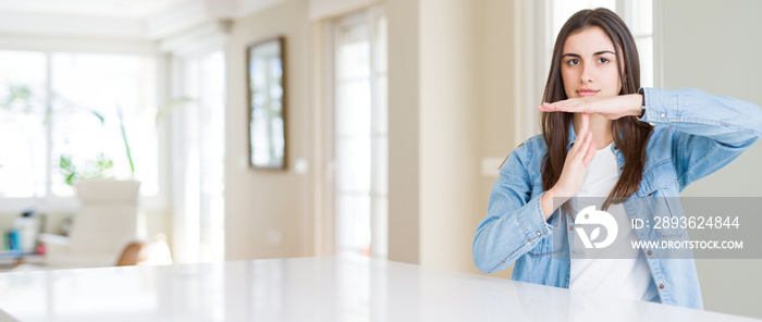 Wide angle picture of beautiful young woman sitting on white table at home Doing time out gesture wi