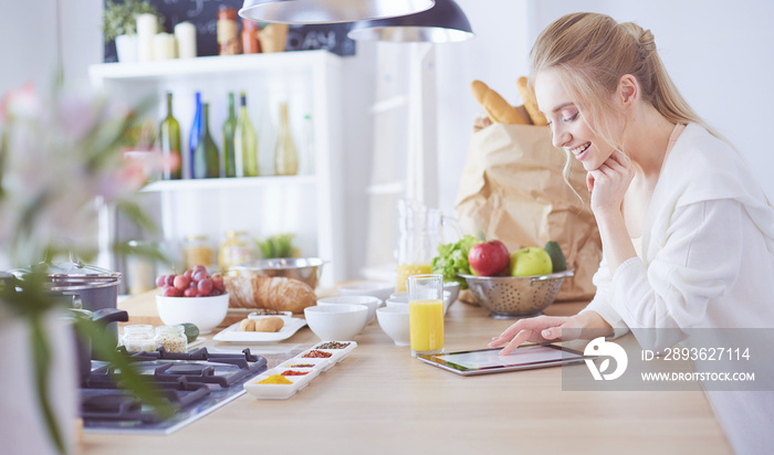 Beautiful young woman using a digital tablet in the kitchen