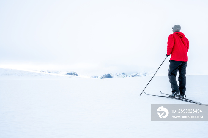 挪威山区雾天，一名身穿红色夹克的男子在越野滑雪，看样子