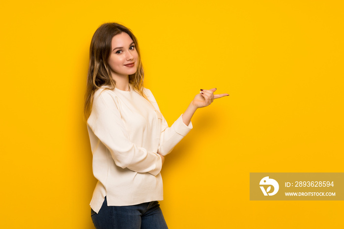 Teenager girl over yellow wall pointing finger to the side in lateral position