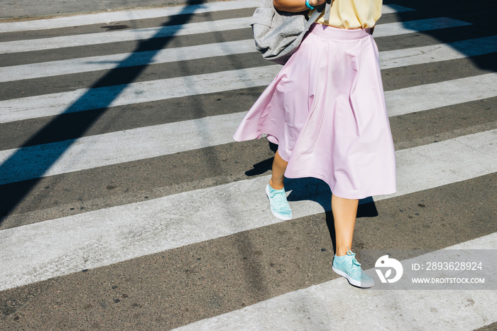 Girl in a pink skirt and sneakers crossing the road in the summe