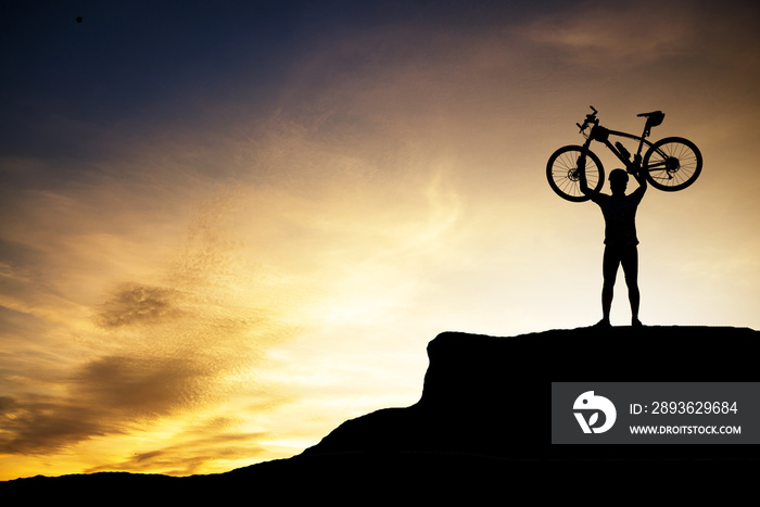 Silhouette of human holding mountain bike on the top of the mountain with beautiful sunset sky.