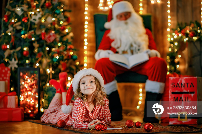 Merry Christmas, santa claus and little child girl at night at the Christmas tree.