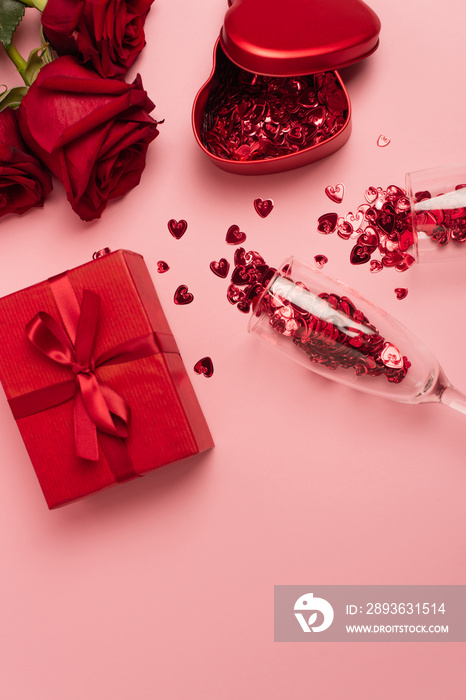 礼盒附近有五彩纸屑心的香槟酒杯和粉红色的红玫瑰的俯视图。