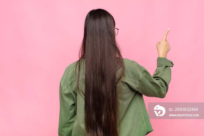 asian young woman standing and pointing to object on copy space, rear view