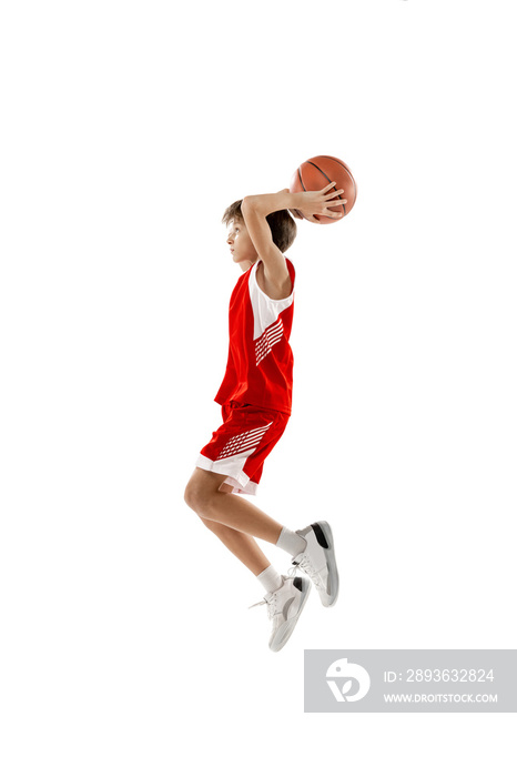 Full-length portrait of teen boy in red uniform training, playing basketball isolated over white bac