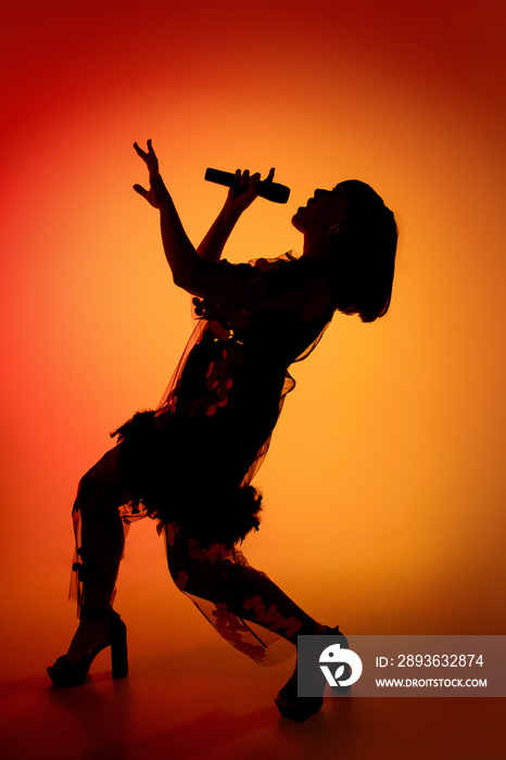 Dance. Silhouette of young female singer isolated on orange gradient studio background in neon light