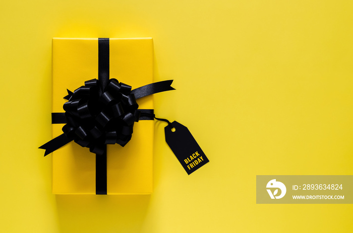 A yellow gift box with black ribbon and price tag puts on yellow background. Black friday concept.