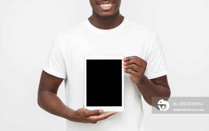 照片中一名年轻的非裔美国男子被隔离在灰色背景下，向vi展示空白平板电脑屏幕