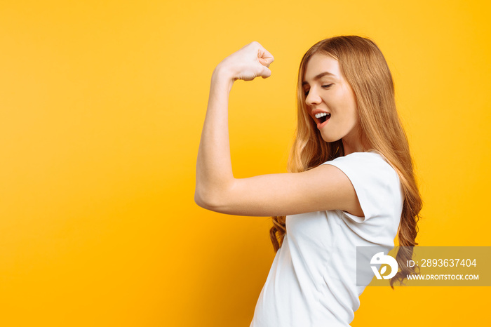 of happy girl in white t-shirt showing arm muscles on yellow background.