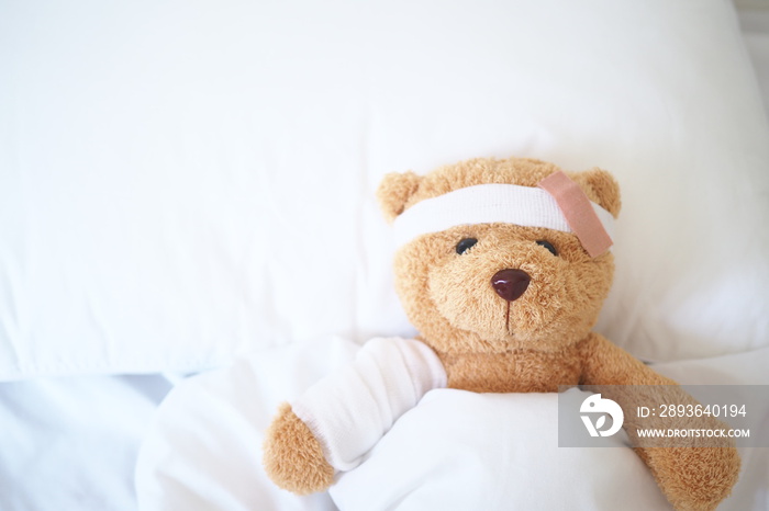 Teddy bear lying sick in bed With a headband and a cloth covered