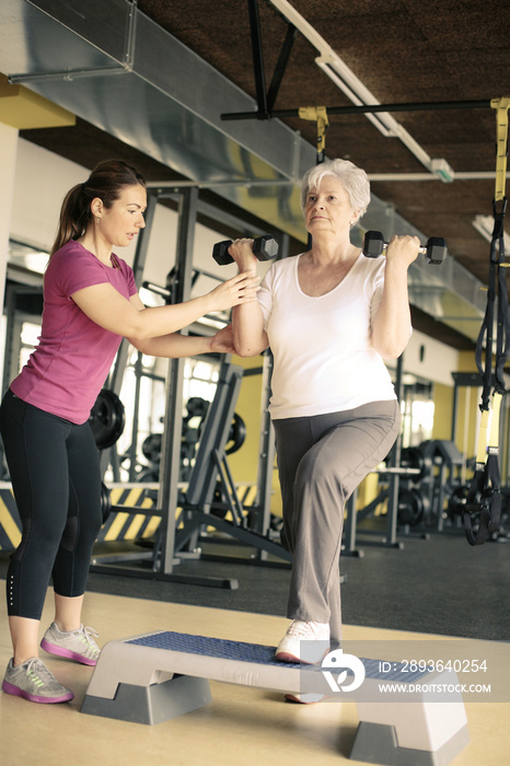 私人教练在健身房与资深女性一起锻炼。资深女性举重。