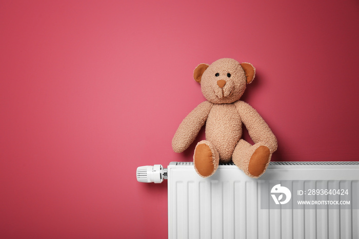 Teddy bear on heating radiator near pink wall