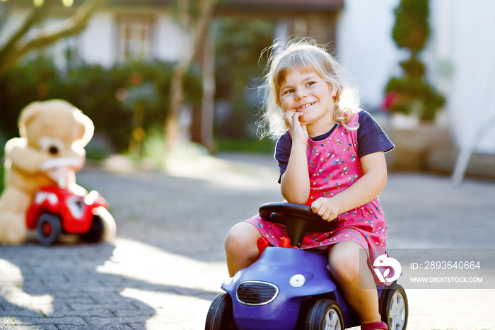 Little adorable toddler girl driving toy car and having fun with playing with plush toy bear, outdoo