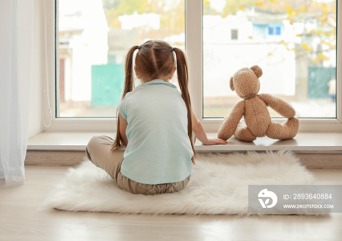 Lonely little girl with teddy bear sitting near window. Autism concept