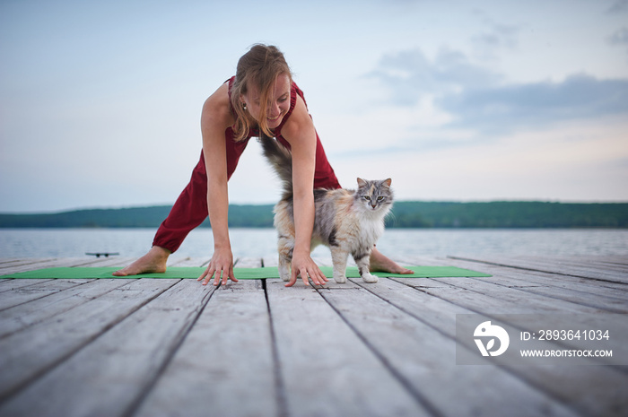 Beautiful young woman practices yoga asana Prasarita Padottanasana on the wooden deck near the lake