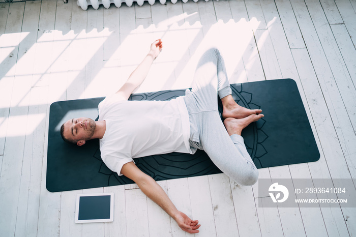 Relaxed man practicing Reclining Bound Angle asana on rubber mat