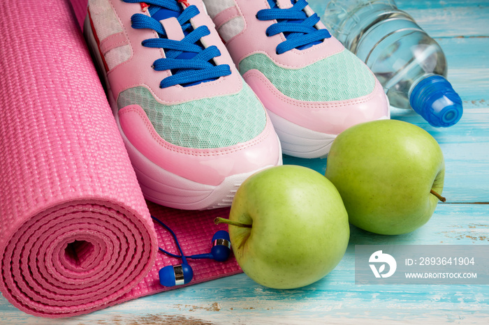 Pink yoga mat, sport shoes, bottle of water and apples on blue wooden background. Sport, healthy lif