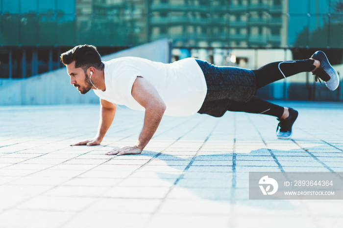 Strong Caucasian sportsman with muscular body shape doing push ups on street enjoying morning workou