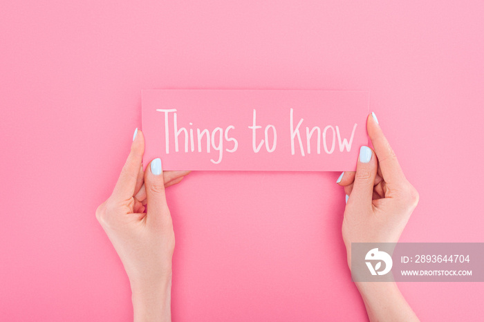 partial view of woman holding pink card with things to know lettering on pink background