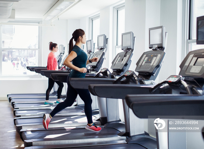 Side view of female athletes exercising on treadmills in gym