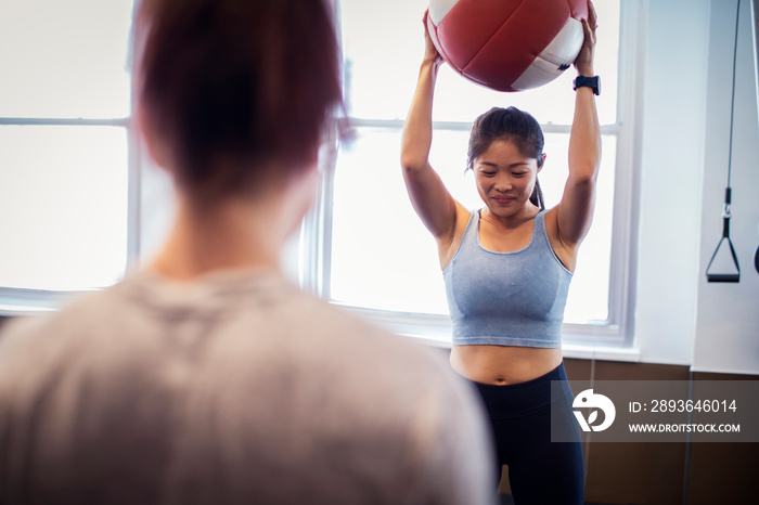 Rear view of female athlete looking at friend exercising with medicine ball while standing against w