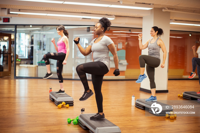 Side view of confident female athletes exercising on aerobic steps in gym