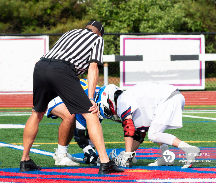 Official standing over two boys during the face off of a lacrosse game