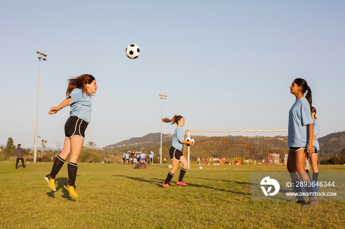 Side view of girls practicing soccer on grassy field against clear blue sky